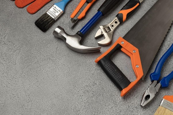 [Obrázok: Rôzne ručné náradie ako kladivo, píla, kľúč a kliešte na sivom povrchu. (freepik)]